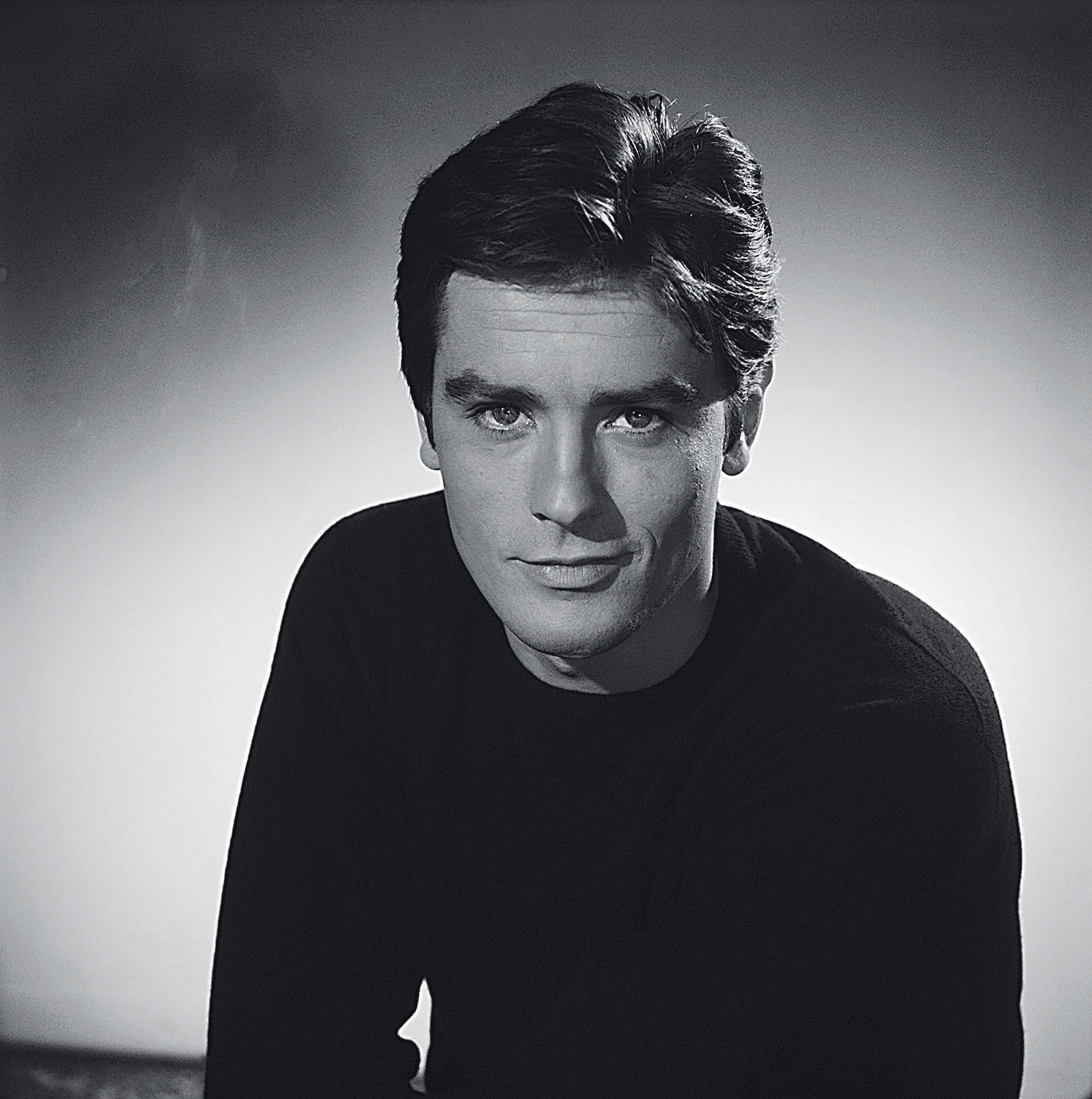 (Original Caption) Head and shoulders portrait photo of French actor Alain Delon (1935-) smiling in a black sweater. Ca. 1960s.