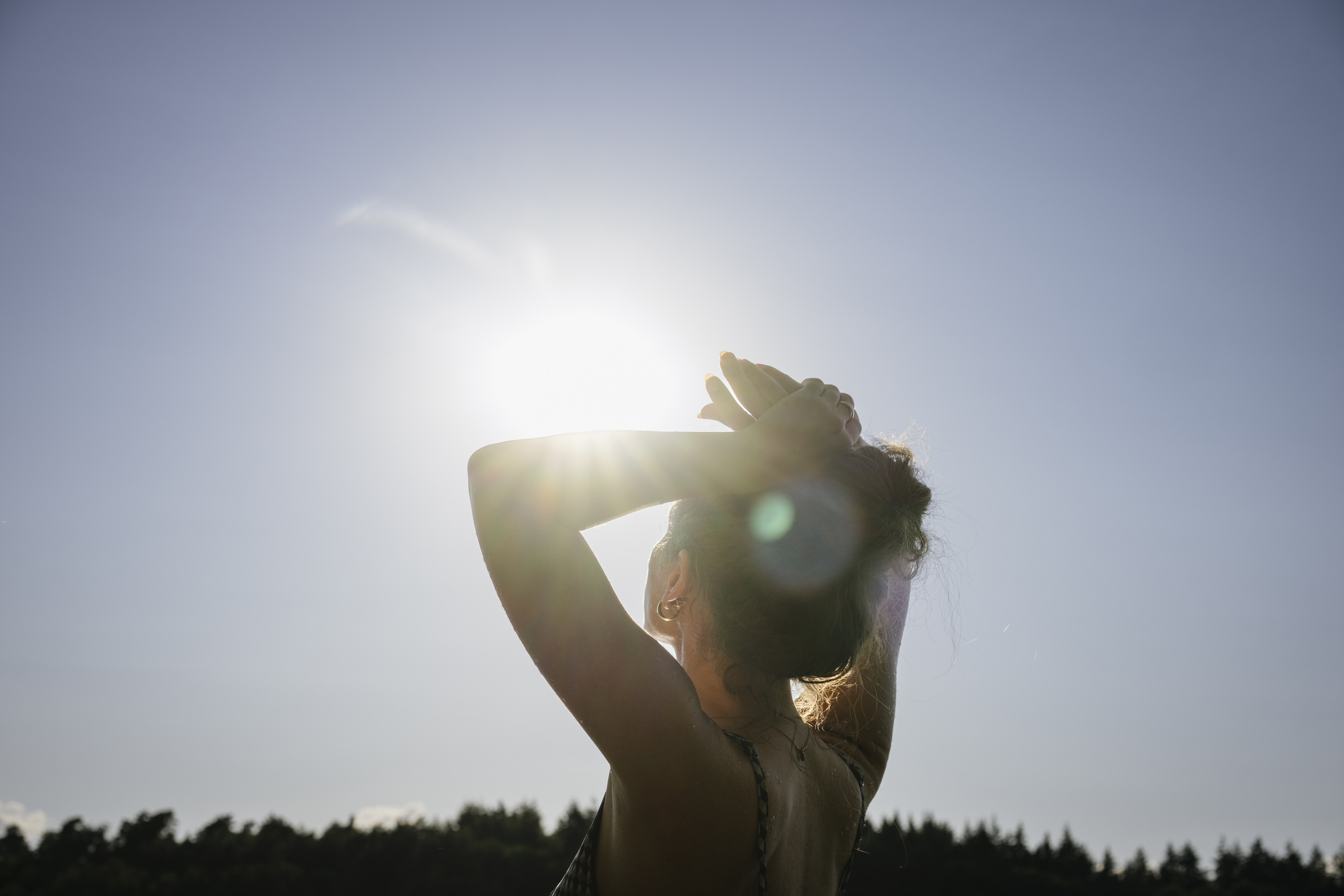 Sunlight shines into the camera while a woman  looks up at the sky
